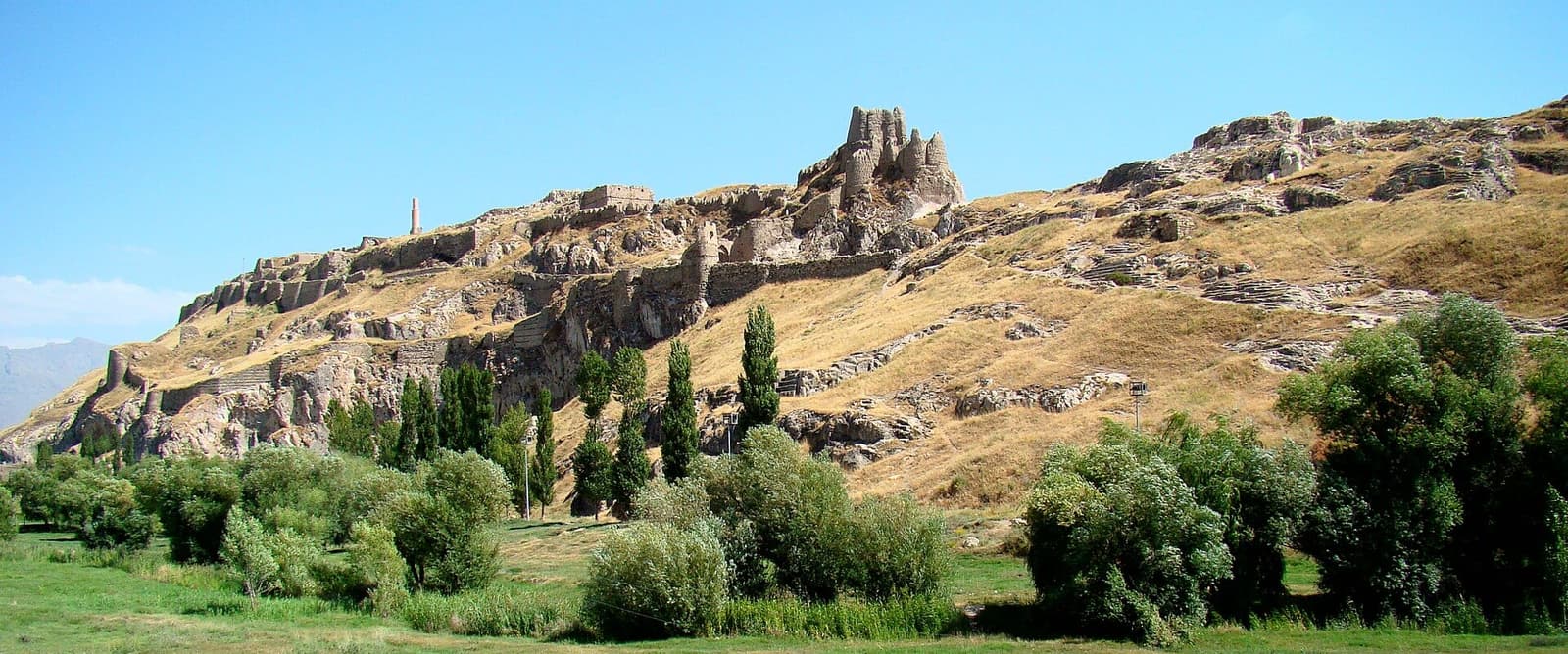 قلعه تاریخی وان بر فراز صخره‌ای بلند با چمنزار و درختان در دامنه
