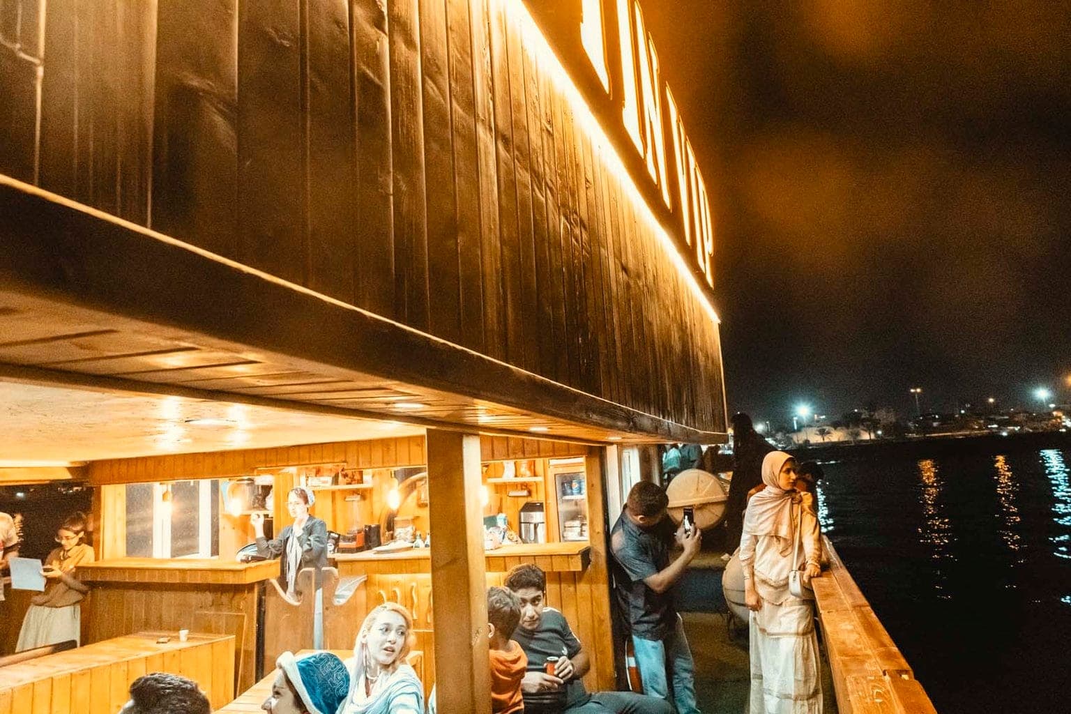 مسافران کنار نردهٔ چوبی عرشهٔ بالایی کشتی آبتین قشم هنگام تماشای منظرهٔ شبانهٔ دریا