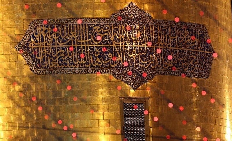 نمای نزدیک گنبد طلایی حرم امام رضا با کتیبه خوشنویسی‌شده در شب