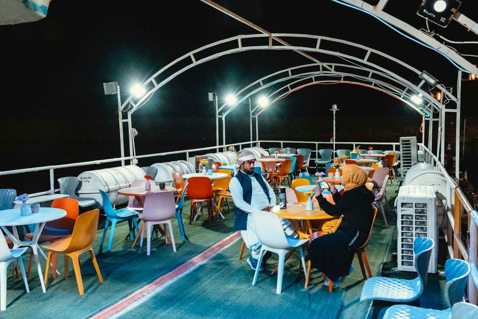 زوج مسافر نشسته دور میز چوبی روی عرشهٔ باز کشتی تارا قشم در شب در حال تماشای عکس‌های گشت
