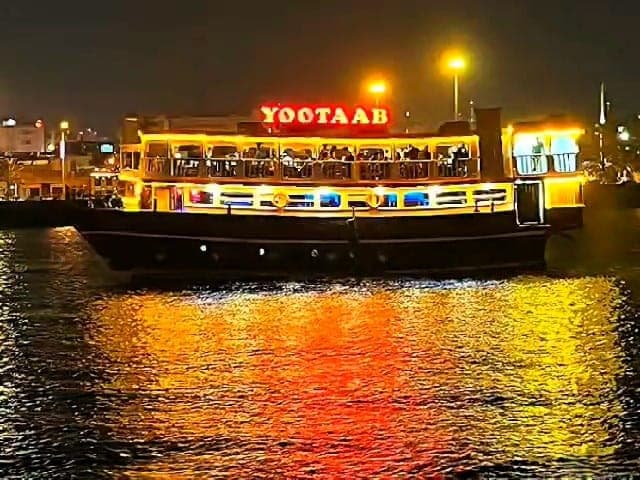 کشتی تفریحی یوتاب قشم وسط آب در شب — نورپردازی کامل طلایی هر دو طبقه و انعکاس نورها روی دریا