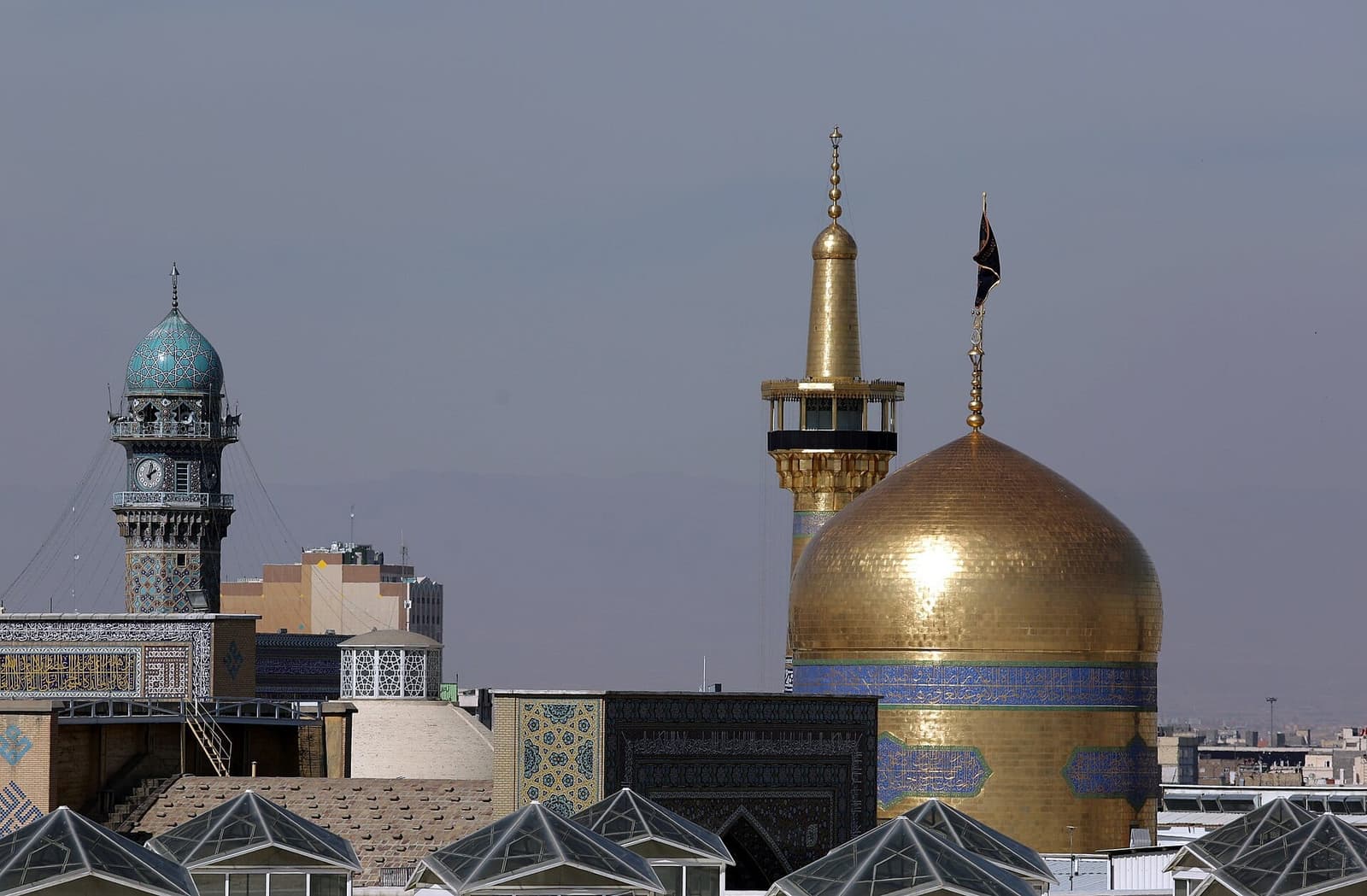 گنبد طلایی و گلدسته زرین حرم امام رضا در کنار مناره فیروزه‌ای در روز