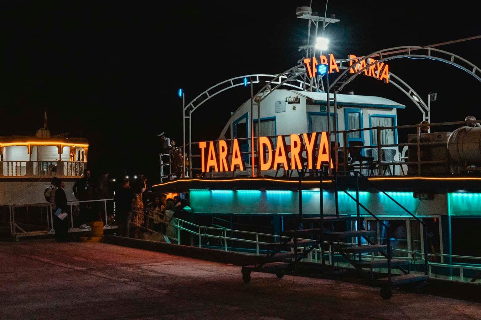 تابلوی نئون نارنجی TARA DARYA روی بدنهٔ کشتی تارا قشم هنگام سوارشدن مسافران از اسکلهٔ ابرکاوان در شب