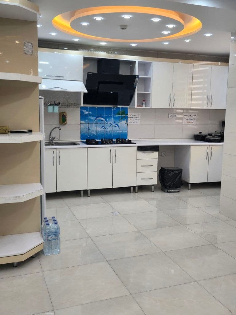آشپزخانه با کابینت سفید و امکانات پخت‌وپز در آپارتمان سجادی قشم