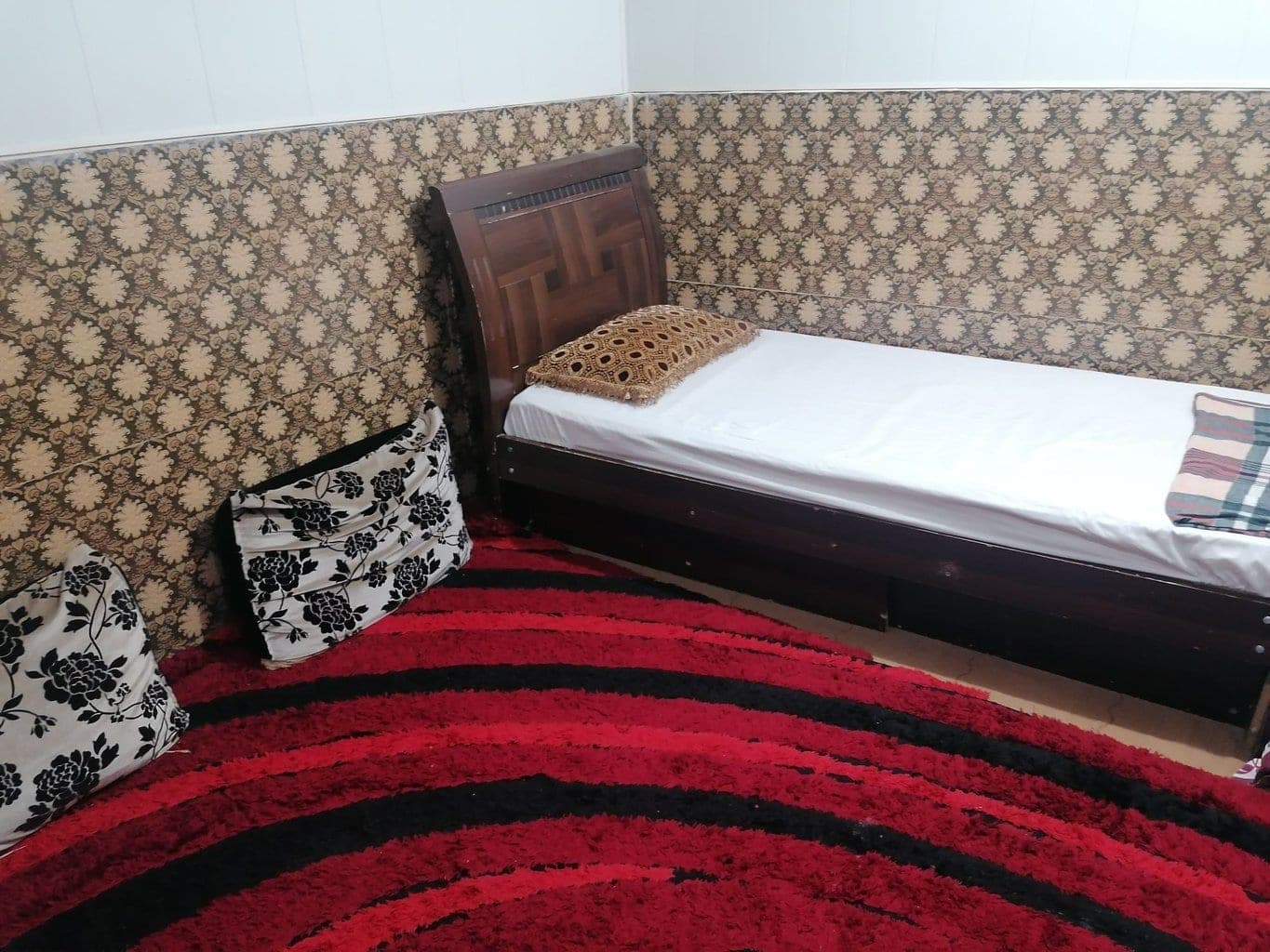 نمای اتاق‌خواب با تخت یک‌نفره و کوسن‌های گل‌دار سوئیت طوفان درگهان قشم