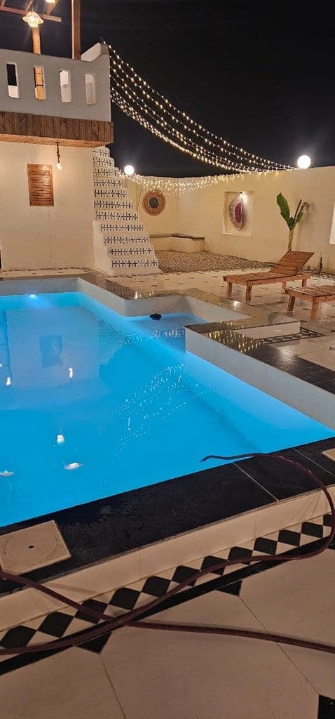 استخر روباز با ریسه‌های نور و تخت آفتاب در شب در ویلا عمارت رستم قشم